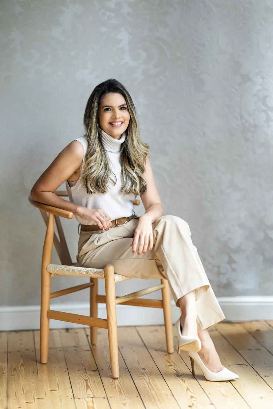 Bruna Maia sentada em uma cadeira de madeira, sorrindo